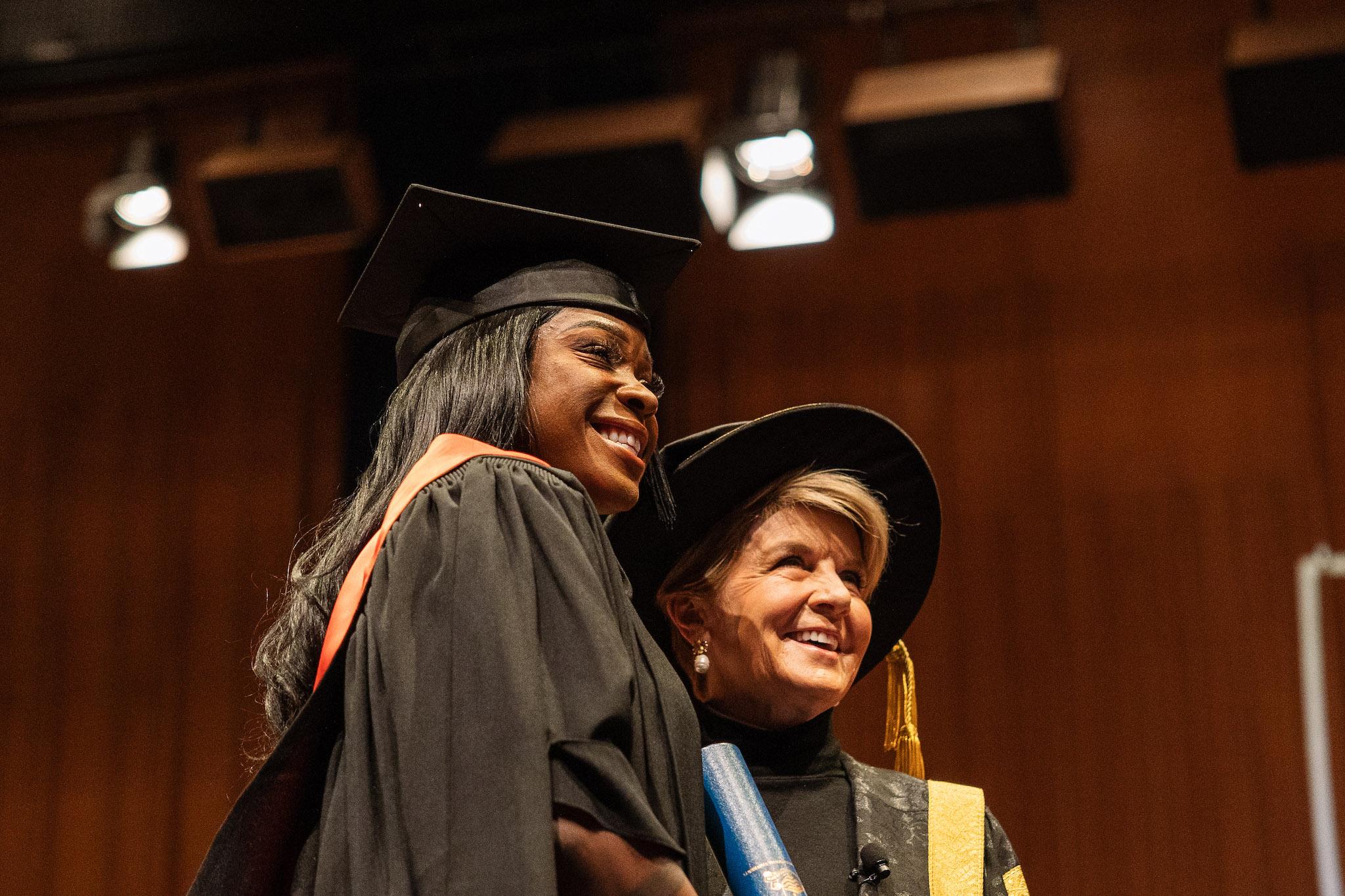 Precilla Anna-Kaii Lawrence standing on stage with Julie Bishop in graduation robes, holding her Testamur