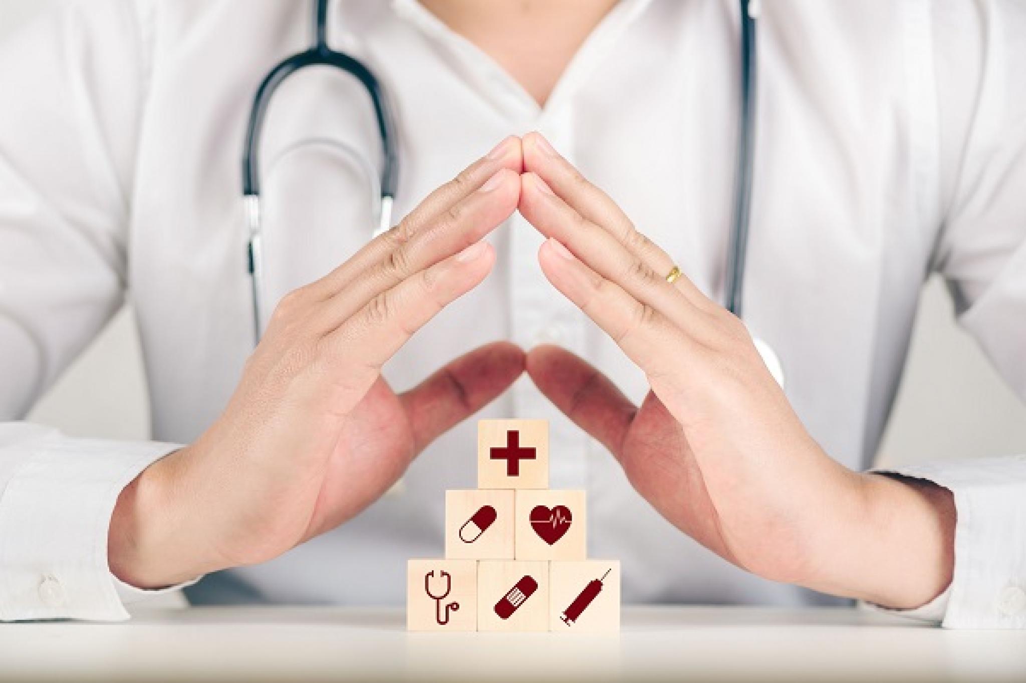 Image of hands of medical professional in a protective gesture over woodblocks with healthcare icons by Deemerwha Studio from Adobe Stock used under Education License 