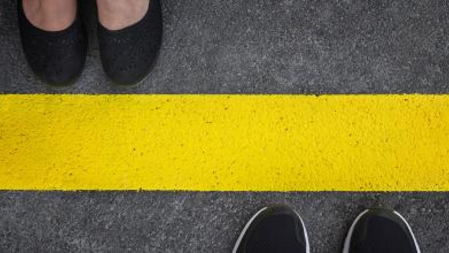 Legs of a couple standing opposite each other divided by the yellow asphalt line top view by adzicnatasa, Adobe Stock